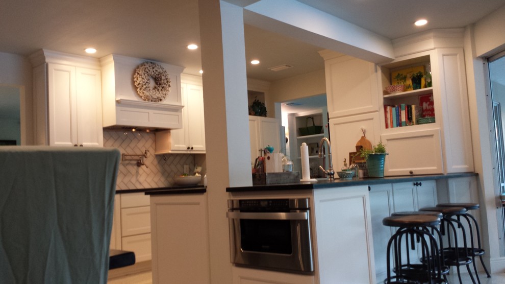 Transitional galley kitchen photo in Tampa with a farmhouse sink, recessed-panel cabinets, white cabinets, granite countertops, beige backsplash, glass tile backsplash and paneled appliances