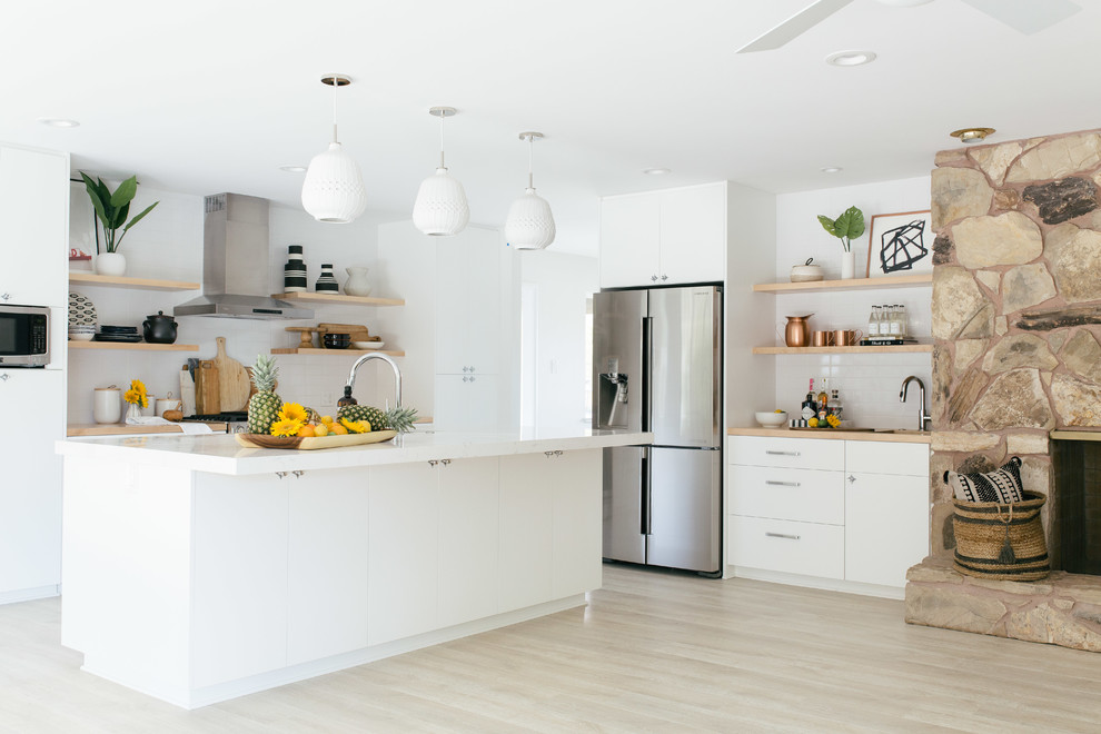 Inspiration for a contemporary l-shaped open plan kitchen in Sacramento with flat-panel cabinets, white cabinets, white splashback, subway tile splashback, stainless steel appliances, light hardwood floors, with island and beige floor.