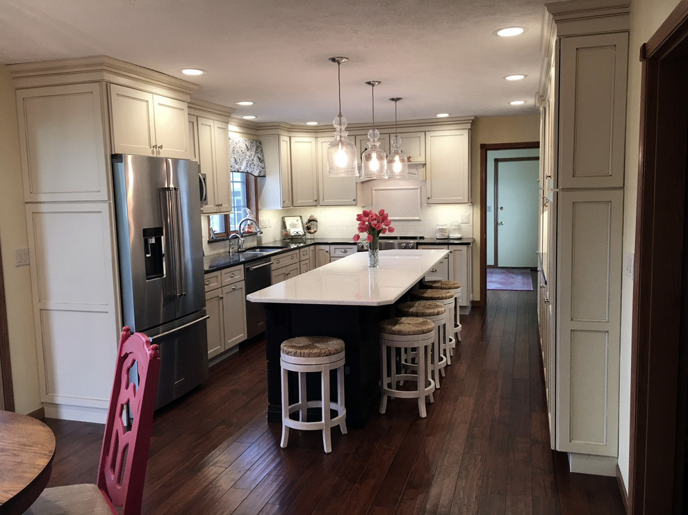 Large transitional medium tone wood floor and brown floor eat-in kitchen photo with an undermount sink, flat-panel cabinets, white cabinets, granite countertops, white backsplash, porcelain backsplash, stainless steel appliances and an island
