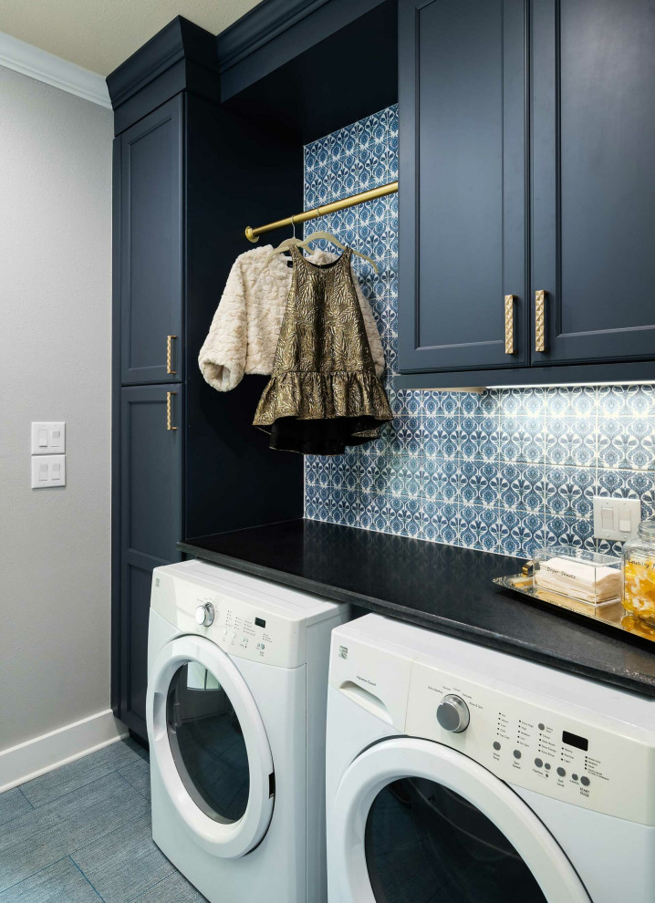 Inspiration for a mid-sized arts and crafts single-wall dedicated laundry room in Dallas with shaker cabinets, blue cabinets, soapstone benchtops, blue splashback, porcelain splashback, grey walls, ceramic floors, a side-by-side washer and dryer, blue floor and black benchtop.