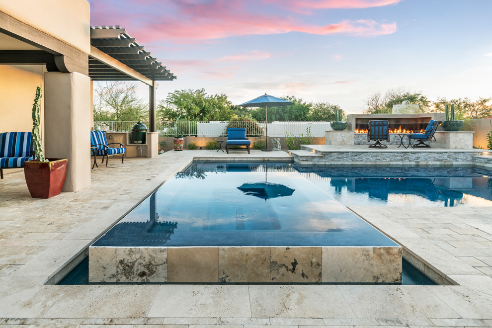 This is an example of a mid-sized contemporary backyard l-shaped infinity pool in Phoenix with natural stone pavers.