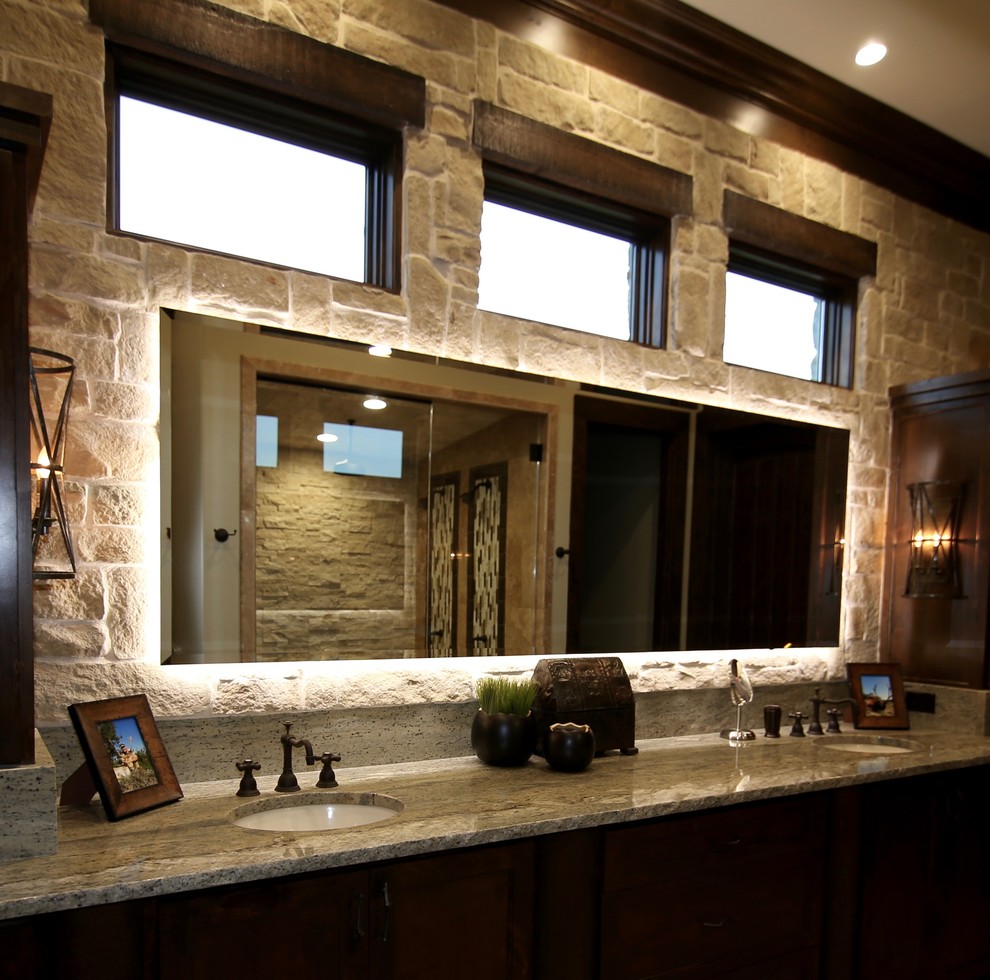 Photo of a mid-sized country master bathroom in Dallas with dark wood cabinets, an undermount sink, granite benchtops, shaker cabinets, travertine floors, an alcove shower, beige tile, stone tile, beige walls, beige floor and a hinged shower door.