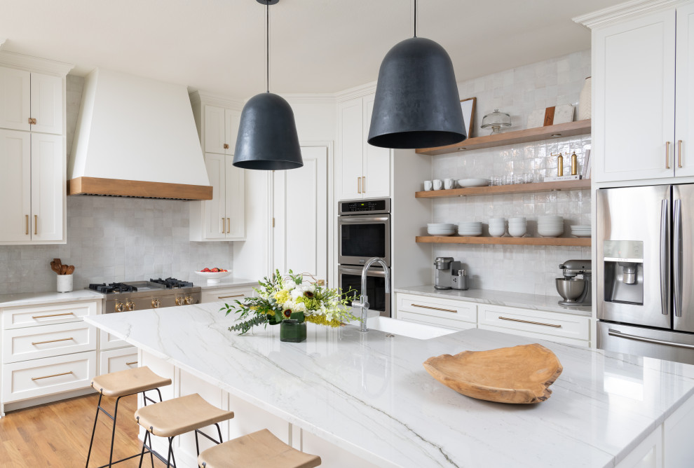 Inspiration for a mid-sized transitional l-shaped open plan kitchen in Dallas with a farmhouse sink, recessed-panel cabinets, white cabinets, quartzite benchtops, white splashback, ceramic splashback, stainless steel appliances, medium hardwood floors, with island and white benchtop.