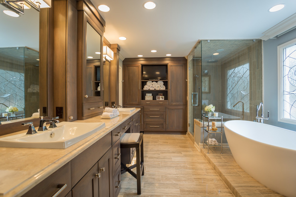 Photo of a large transitional master bathroom in Atlanta with recessed-panel cabinets, brown cabinets, a japanese tub, a corner shower, beige tile, stone tile, blue walls, ceramic floors, granite benchtops, an integrated sink, brown floor, a hinged shower door, beige benchtops, a double vanity and a built-in vanity.