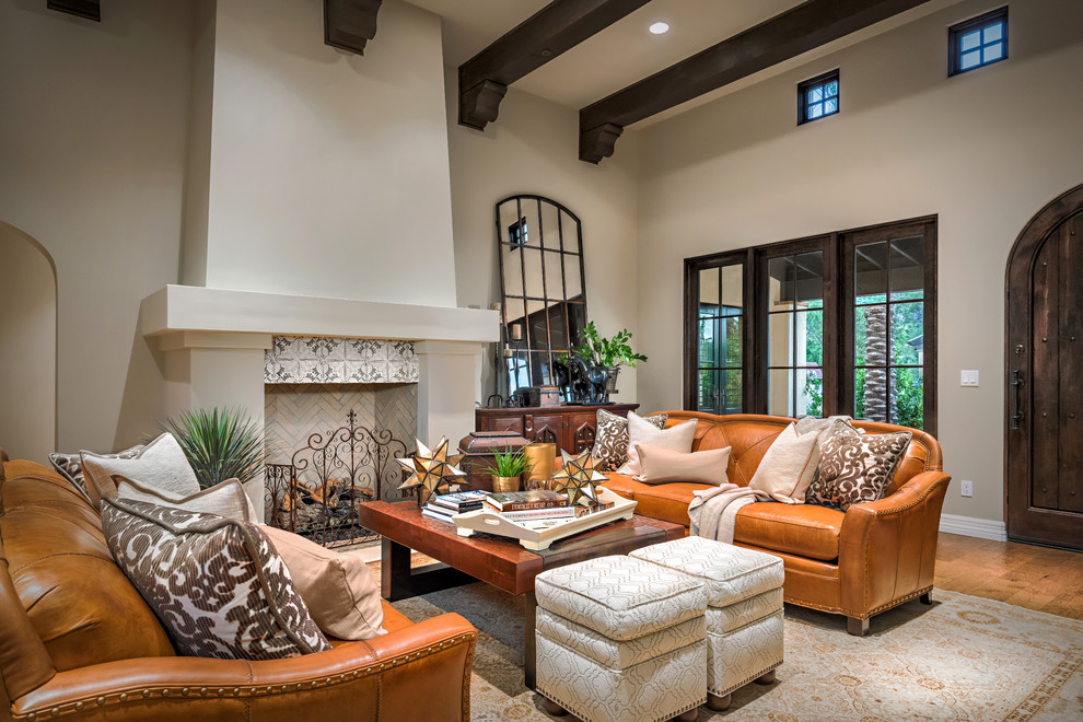 Photo of a large mediterranean open concept living room in Phoenix with a standard fireplace, a tile fireplace surround, beige walls, medium hardwood floors and brown floor.