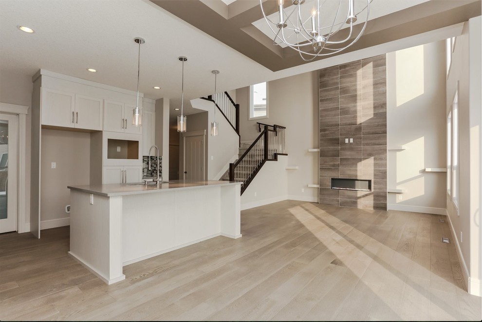 Mid-sized traditional l-shaped open plan kitchen in Edmonton with recessed-panel cabinets, white cabinets, stainless steel appliances, light hardwood floors, with island and brown floor.