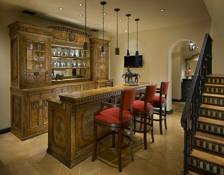 This is an example of a large mediterranean galley seated home bar in Phoenix with glass-front cabinets, dark wood cabinets, wood benchtops, mirror splashback, ceramic floors and brown benchtop.