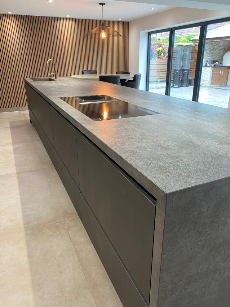 Design ideas for a large contemporary galley open plan kitchen in Manchester with an undermount sink, flat-panel cabinets, grey cabinets, quartz benchtops, metallic splashback, black appliances, porcelain floors, with island, beige floor, grey benchtop and vaulted.