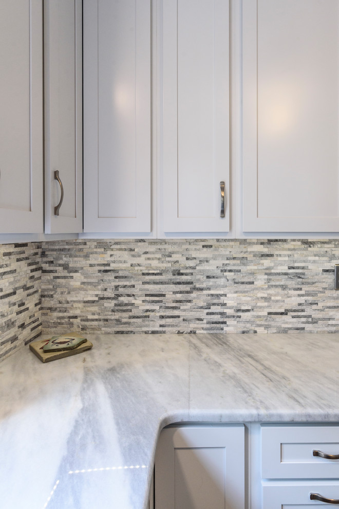 Inspiration for a large transitional l-shaped ceramic tile and brown floor home design remodel in Baltimore with a farmhouse sink, shaker cabinets, white cabinets, granite countertops, gray backsplash, stone tile backsplash, stainless steel appliances, no island and white countertops