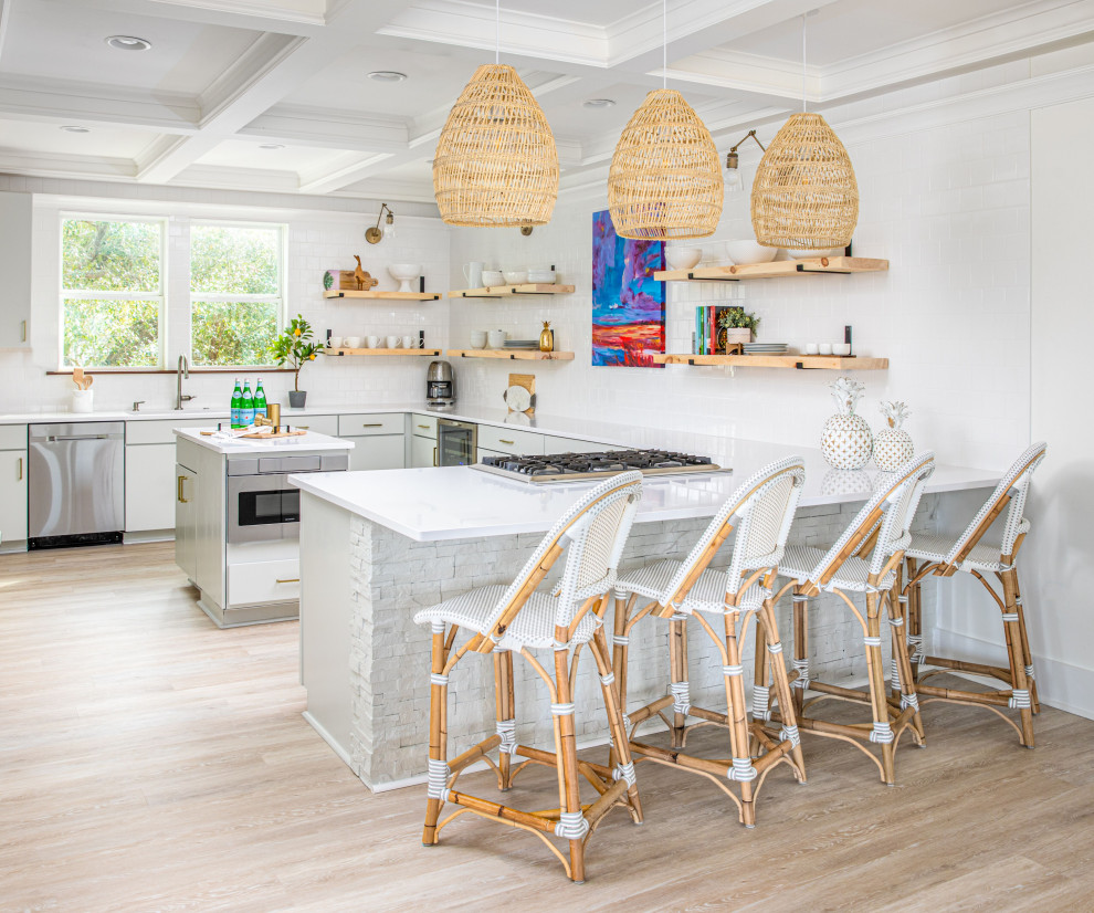 Photo of a beach style kitchen in Charleston with an undermount sink, flat-panel cabinets, grey cabinets, white splashback, subway tile splashback, stainless steel appliances, light hardwood floors, a peninsula, beige floor, white benchtop and coffered.