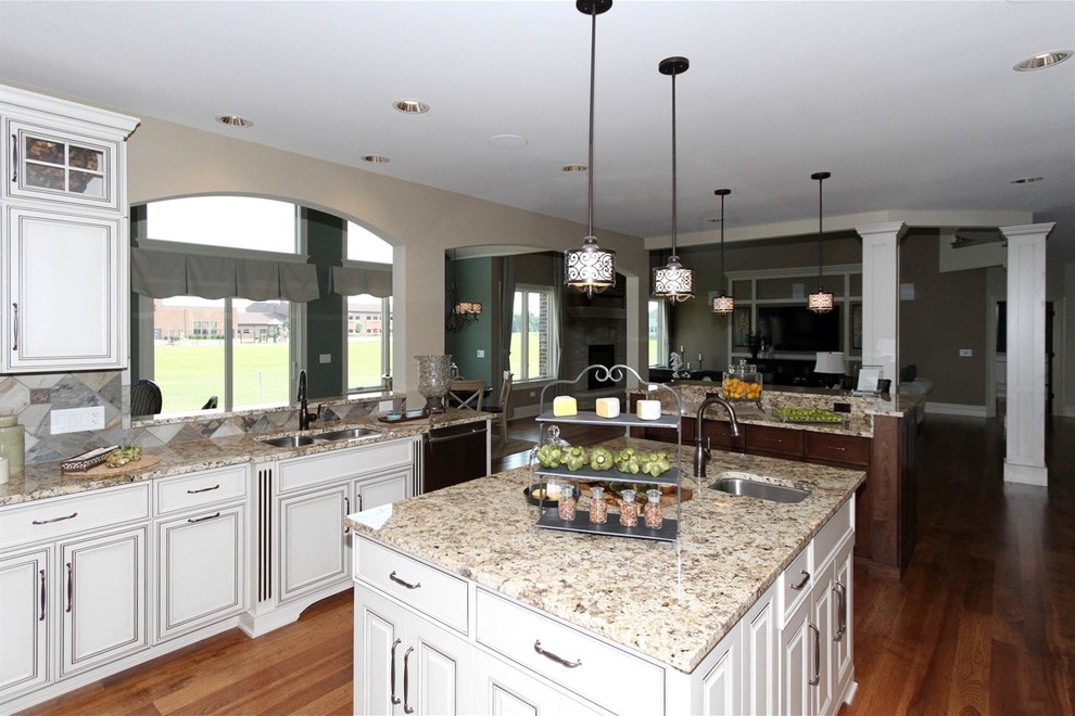 Inspiration for a large transitional u-shaped medium tone wood floor eat-in kitchen remodel in Chicago with a double-bowl sink, raised-panel cabinets, distressed cabinets, granite countertops, stainless steel appliances and two islands