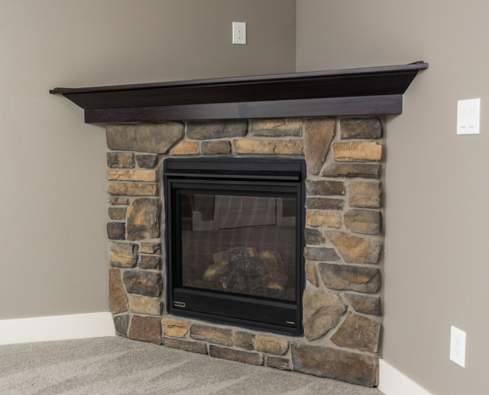 Example of a large transitional walk-out carpeted basement design with gray walls, a corner fireplace and a stone fireplace