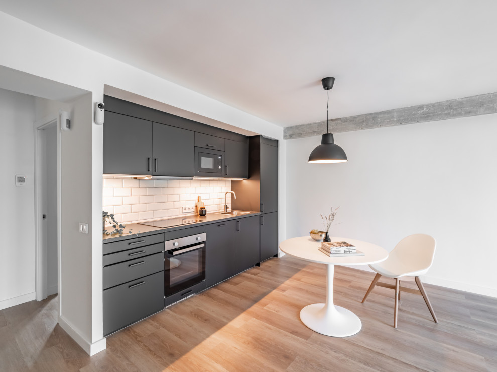 Design ideas for a small modern grey and white single-wall open plan kitchen in Madrid with a single-bowl sink, flat-panel cabinets, grey cabinets, laminate countertops, white splashback, metro tiled splashback, black appliances, laminate floors, no island, brown floors and grey worktops.