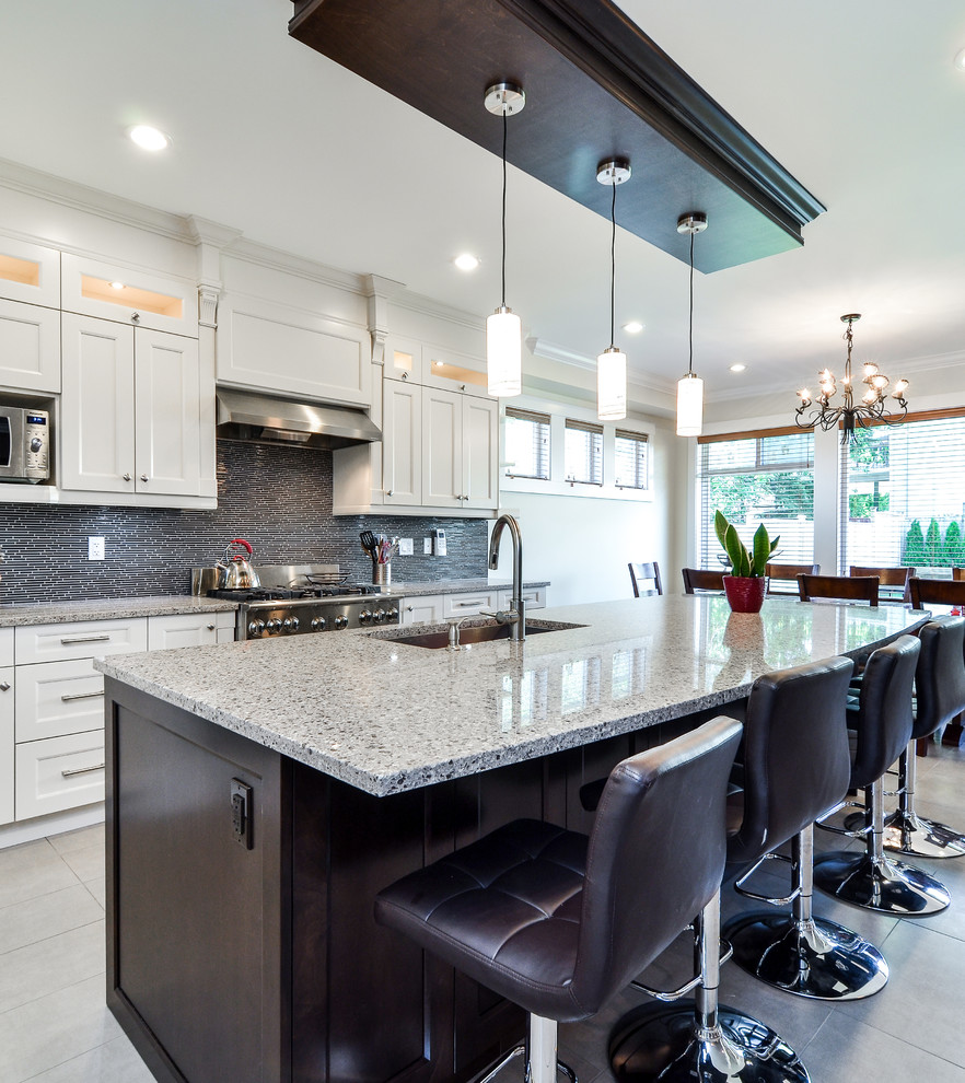 This is an example of a large modern l-shaped eat-in kitchen in Vancouver with shaker cabinets, with island, white cabinets, an undermount sink, quartzite benchtops, black splashback, matchstick tile splashback, stainless steel appliances and limestone floors.