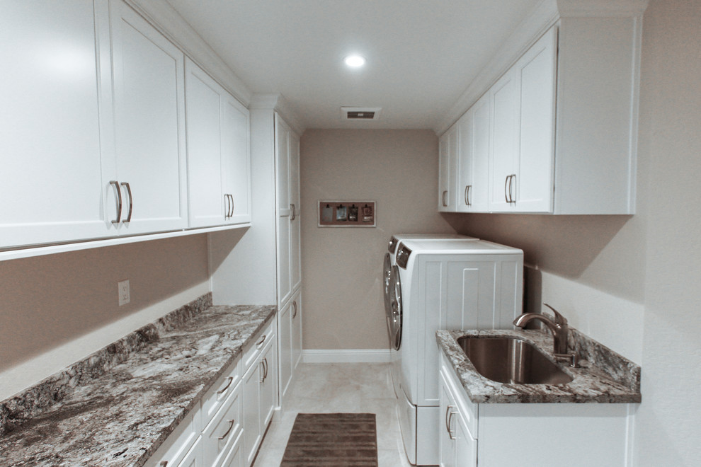 This is an example of a mid-sized traditional galley dedicated laundry room in San Francisco with an undermount sink, white cabinets, granite benchtops, beige splashback, marble splashback, recessed-panel cabinets, beige walls, porcelain floors, a side-by-side washer and dryer and beige floor.