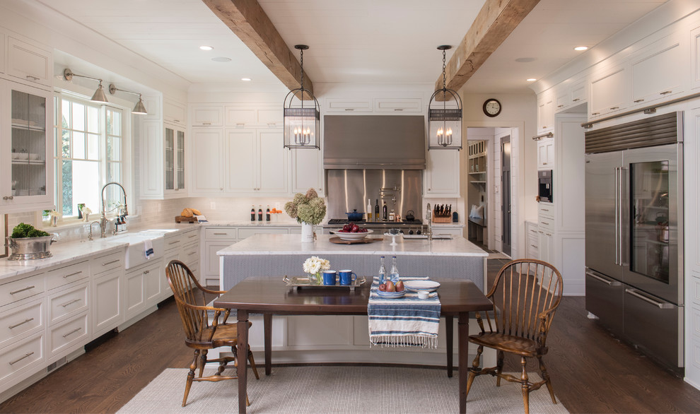 Photo of a traditional u-shaped eat-in kitchen in Atlanta with a farmhouse sink, recessed-panel cabinets, white cabinets, white splashback, stainless steel appliances, dark hardwood floors, brown floor and white benchtop.