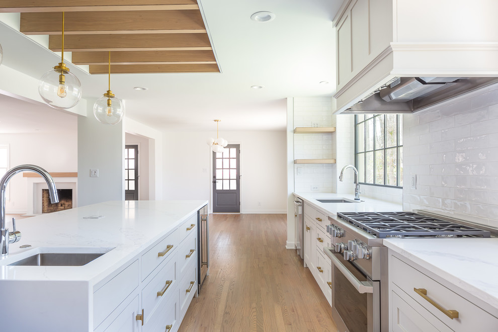 Large contemporary l-shaped separate kitchen in Raleigh with an undermount sink, shaker cabinets, white cabinets, marble benchtops, white splashback, porcelain splashback, stainless steel appliances, light hardwood floors, with island, brown floor and white benchtop.