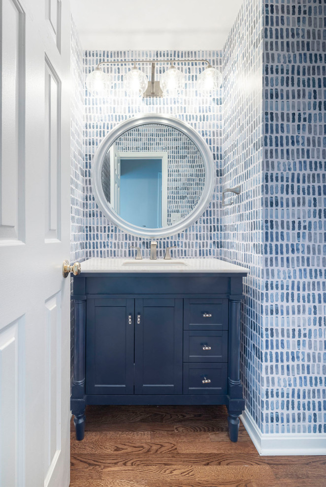 Small coastal cloakroom in DC Metro with freestanding cabinets, blue cabinets, a one-piece toilet, blue tiles, multi-coloured walls, medium hardwood flooring, a submerged sink, engineered stone worktops, brown floors, white worktops, a freestanding vanity unit and wallpapered walls.