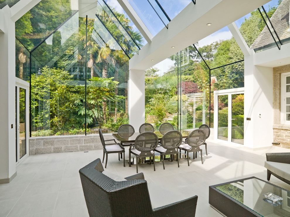 Large contemporary sunroom in Cornwall with no fireplace, beige floor, limestone floors and a glass ceiling.