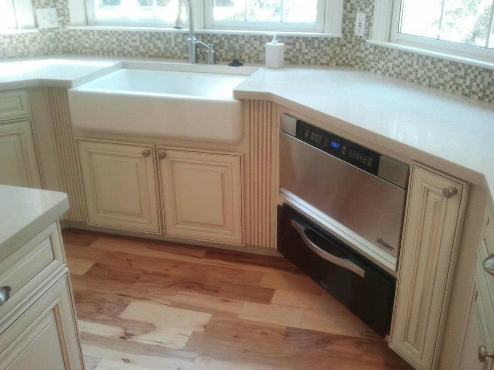 Mid-sized medium tone wood floor kitchen photo with a farmhouse sink, raised-panel cabinets, white cabinets, solid surface countertops, multicolored backsplash, mosaic tile backsplash, stainless steel appliances and an island