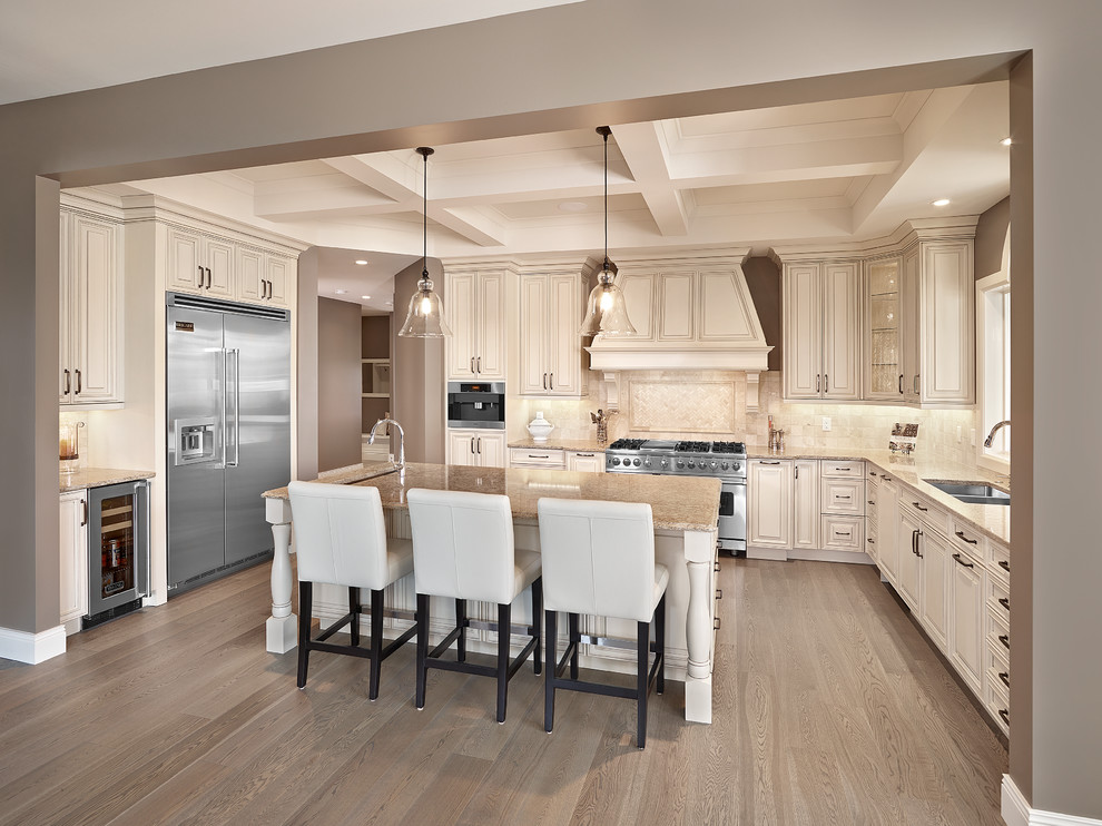 This is an example of a large traditional u-shaped kitchen in Edmonton with an undermount sink, raised-panel cabinets, beige cabinets, quartz benchtops, beige splashback, stone tile splashback, stainless steel appliances, medium hardwood floors and with island.