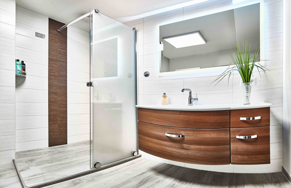 This is an example of a small contemporary bathroom in Leipzig with flat-panel cabinets, dark wood cabinets, a corner shower, a wall-mount toilet, white tile, white walls, an integrated sink and a sliding shower screen.