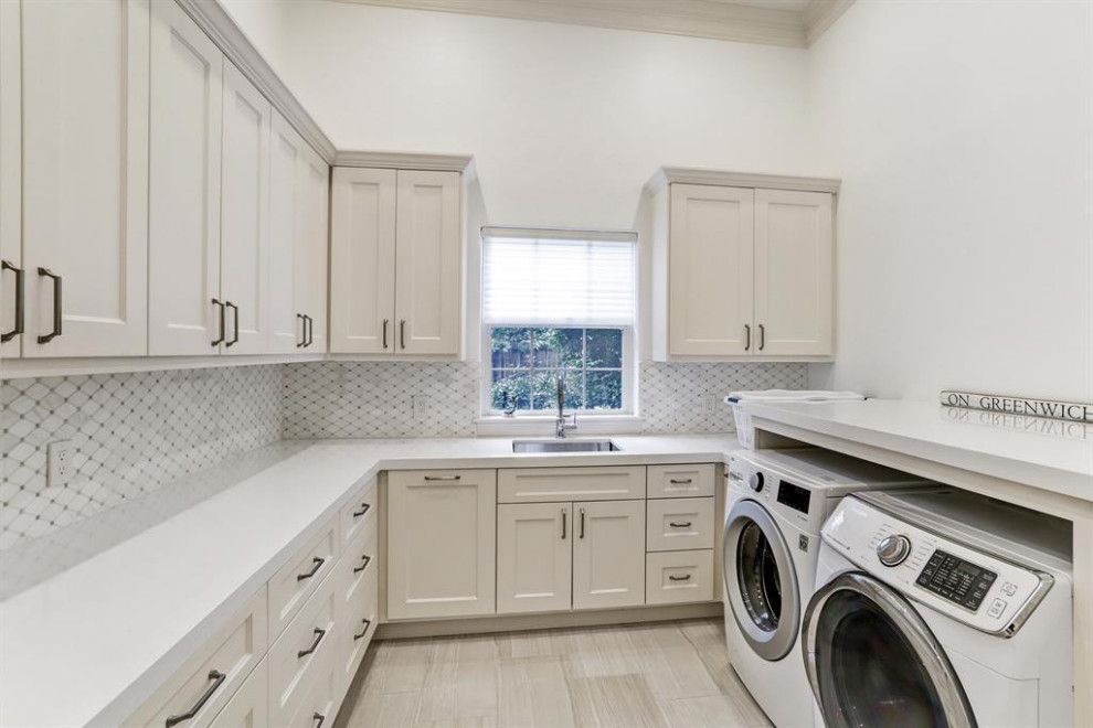 This is an example of a mid-sized transitional u-shaped dedicated laundry room in Houston with an undermount sink, beige cabinets, quartz benchtops, white walls, porcelain floors, an integrated washer and dryer, beige floor, white benchtop and recessed-panel cabinets.