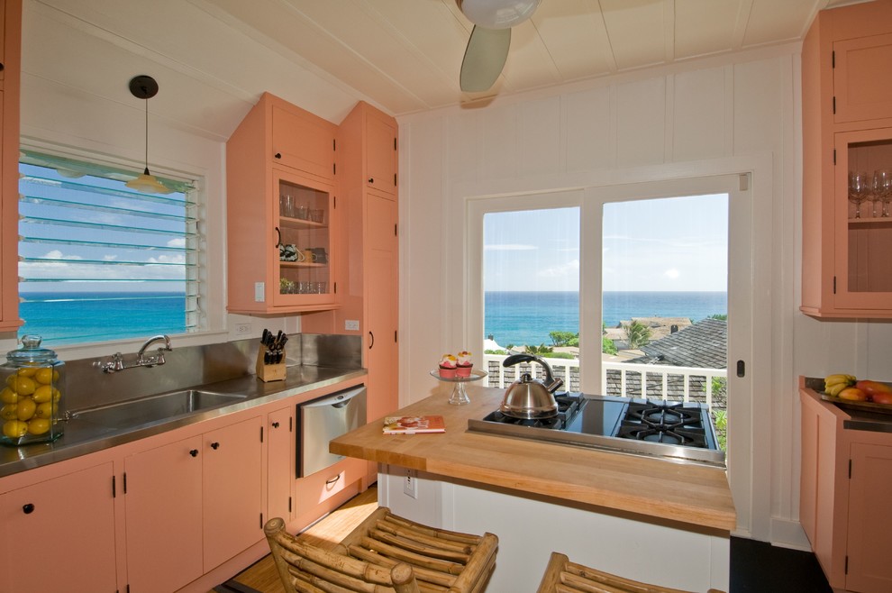 This is an example of a mid-sized beach style u-shaped separate kitchen in Santa Barbara with an integrated sink, beaded inset cabinets, orange cabinets, stainless steel benchtops, metallic splashback, metal splashback, stainless steel appliances, medium hardwood floors and with island.