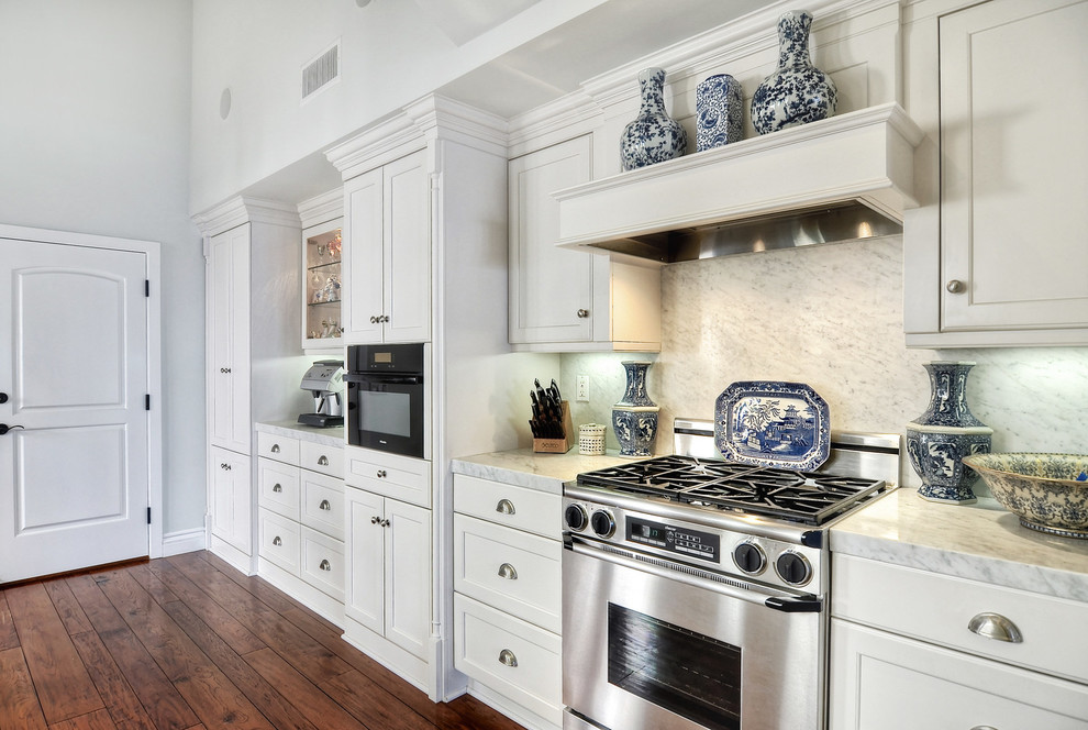 Design ideas for a mid-sized traditional galley kitchen pantry in Orange County with a farmhouse sink, recessed-panel cabinets, white cabinets, marble benchtops, multi-coloured splashback, stone slab splashback, stainless steel appliances, medium hardwood floors and no island.