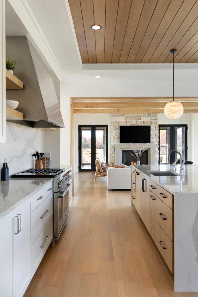 Inspiration for a country eat-in kitchen in Minneapolis with an undermount sink, flat-panel cabinets, white cabinets, quartz benchtops, white splashback, engineered quartz splashback, stainless steel appliances, light hardwood floors, with island, brown floor, white benchtop and timber.