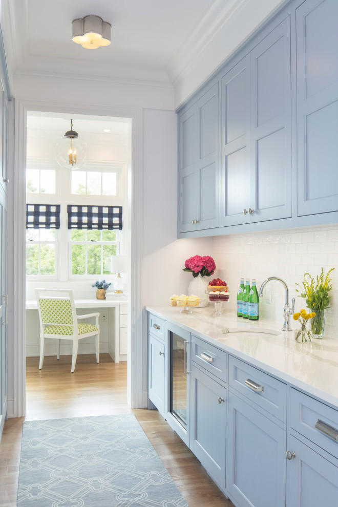 This is an example of a small transitional galley kitchen pantry in Minneapolis with an undermount sink, recessed-panel cabinets, blue cabinets, quartz benchtops, white splashback, subway tile splashback, panelled appliances, medium hardwood floors, no island, brown floor and white benchtop.