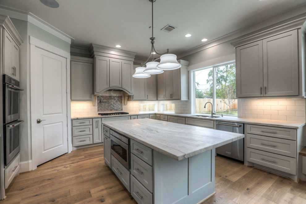 Inspiration for a mid-sized transitional u-shaped light wood floor and beige floor enclosed kitchen remodel in Houston with shaker cabinets, gray cabinets, white backsplash, stainless steel appliances, an island, a double-bowl sink, quartz countertops and subway tile backsplash