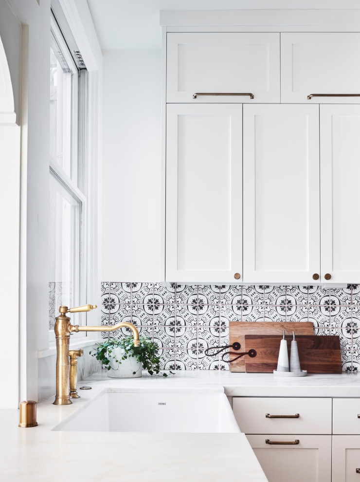 Design ideas for a mid-sized scandinavian u-shaped separate kitchen in San Francisco with a farmhouse sink, shaker cabinets, white cabinets, marble benchtops, multi-coloured splashback, cement tile splashback, stainless steel appliances, light hardwood floors, a peninsula, brown floor and white benchtop.