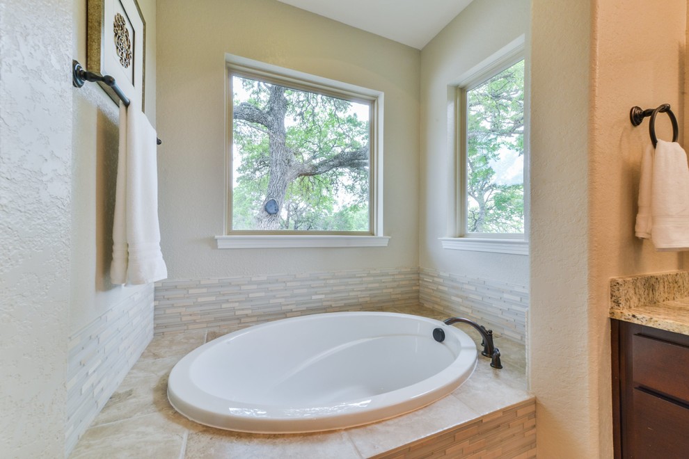 Example of a large transitional master beige tile and glass tile drop-in bathtub design in Austin with dark wood cabinets, beige walls and granite countertops