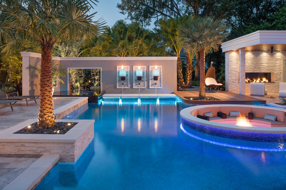 This is an example of a large modern backyard custom-shaped pool in Tampa with natural stone pavers and a pool house.