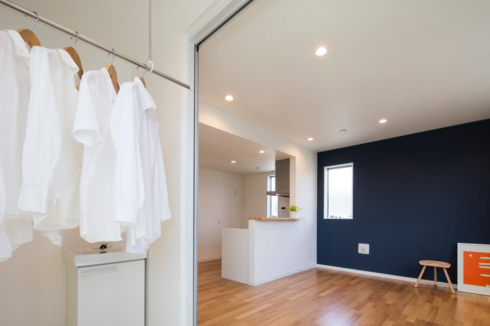 This is an example of a mid-sized modern utility room in Tokyo with white walls, ceramic floors, an integrated washer and dryer, beige floor, wallpaper and wallpaper.
