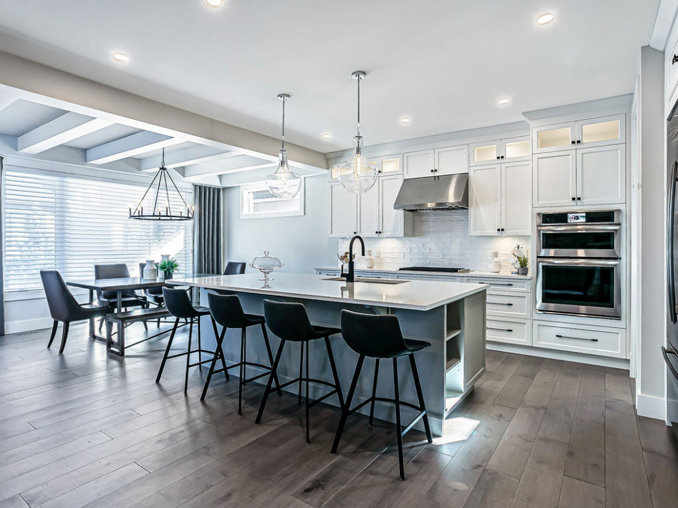 Inspiration for a transitional l-shaped light wood floor and gray floor eat-in kitchen remodel in Calgary with a double-bowl sink, shaker cabinets, gray cabinets, quartz countertops, white backsplash, ceramic backsplash, stainless steel appliances, an island and white countertops