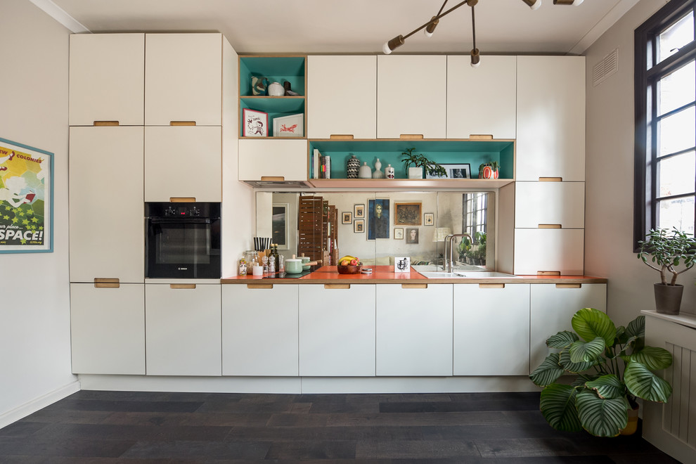 Design ideas for a small eclectic single-wall open plan kitchen in London with flat-panel cabinets, white cabinets, laminate benchtops, mirror splashback, dark hardwood floors, no island, a drop-in sink, black appliances, black floor and orange benchtop.