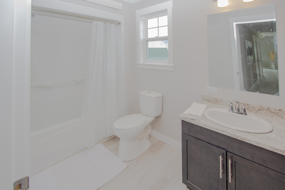 На фото: детская ванная комната среднего размера в классическом стиле с фасадами в стиле шейкер, серыми фасадами, ванной в нише, душем в нише, унитазом-моноблоком, бежевой плиткой, бежевыми стенами, полом из ламината, накладной раковиной, столешницей из ламината, бежевым полом, шторкой для ванной, бежевой столешницей, тумбой под одну раковину и встроенной тумбой