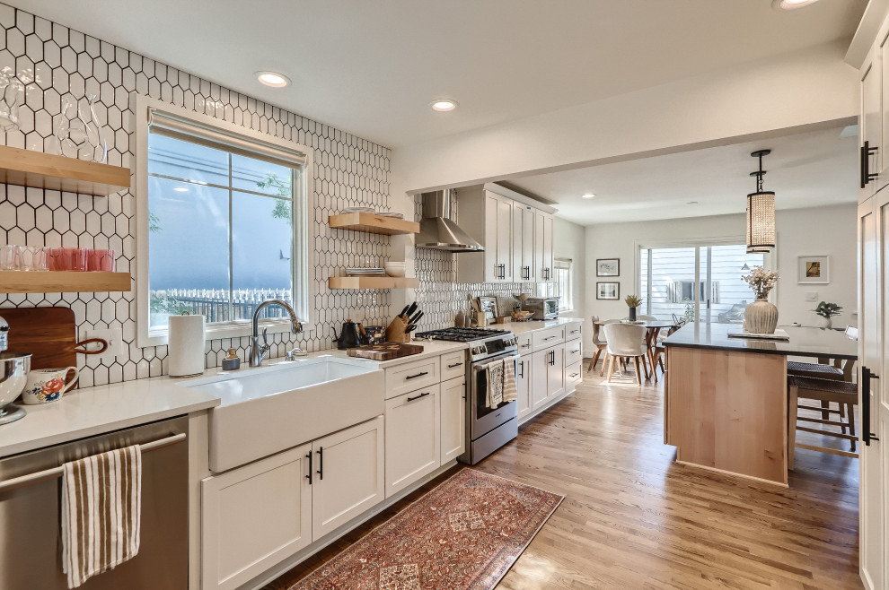 Large minimalist galley medium tone wood floor and beige floor kitchen photo in Denver with a farmhouse sink, shaker cabinets, white cabinets, quartz countertops, white backsplash, ceramic backsplash, stainless steel appliances, an island and white countertops