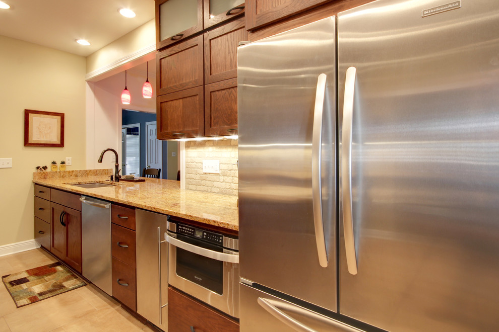 Eat-in kitchen - transitional eat-in kitchen idea in Miami with an undermount sink, shaker cabinets, brown cabinets, granite countertops, beige backsplash, stone tile backsplash and stainless steel appliances