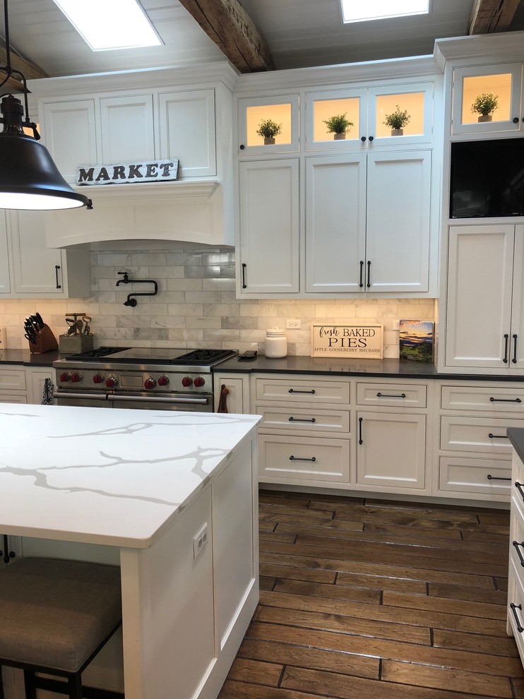 Inspiration for a large country single-wall eat-in kitchen in Chicago with a farmhouse sink, shaker cabinets, white cabinets, grey splashback, stainless steel appliances, dark hardwood floors, with island, brown floor, black benchtop, quartzite benchtops and marble splashback.
