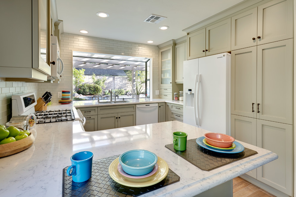 This is an example of a traditional u-shaped kitchen in Sacramento with a double-bowl sink, shaker cabinets, green cabinets, quartz benchtops, glass tile splashback, white appliances and grey splashback.