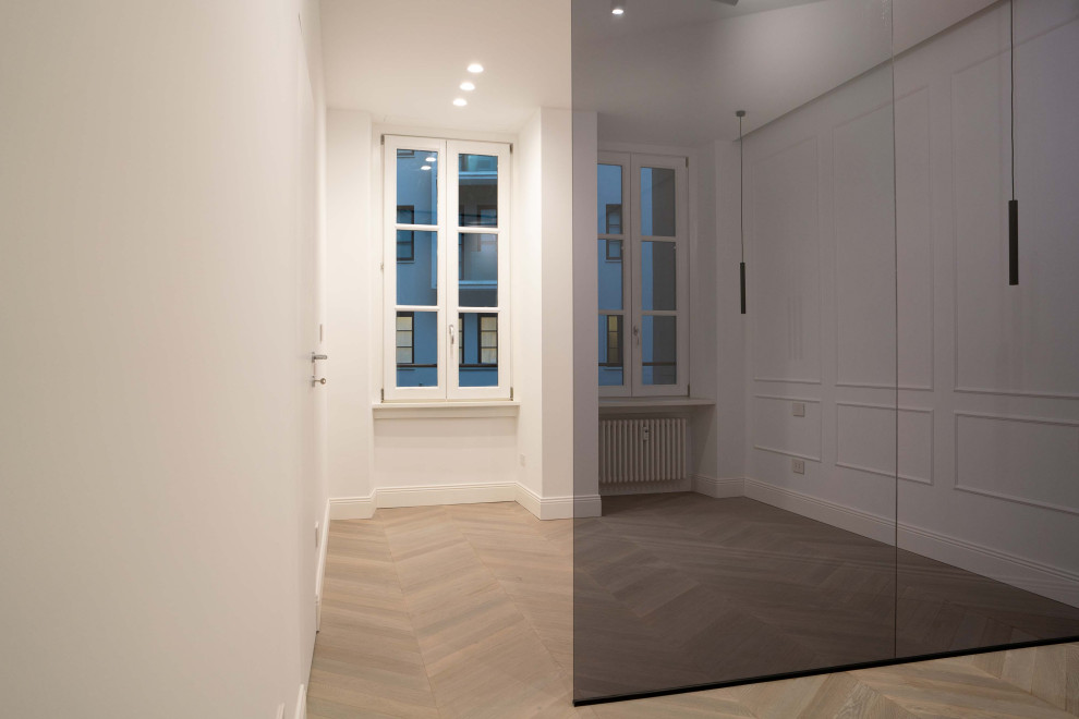Ejemplo de dormitorio principal moderno de tamaño medio con paredes blancas, suelo de madera clara y boiserie