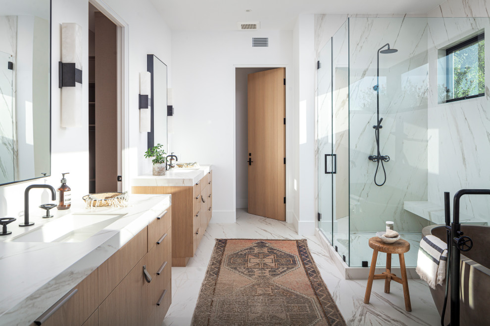 This is an example of a contemporary master bathroom in Orange County with flat-panel cabinets, medium wood cabinets, a freestanding tub, a corner shower, white tile, stone slab, white walls, an undermount sink, white floor, a hinged shower door, white benchtops, a double vanity and a built-in vanity.