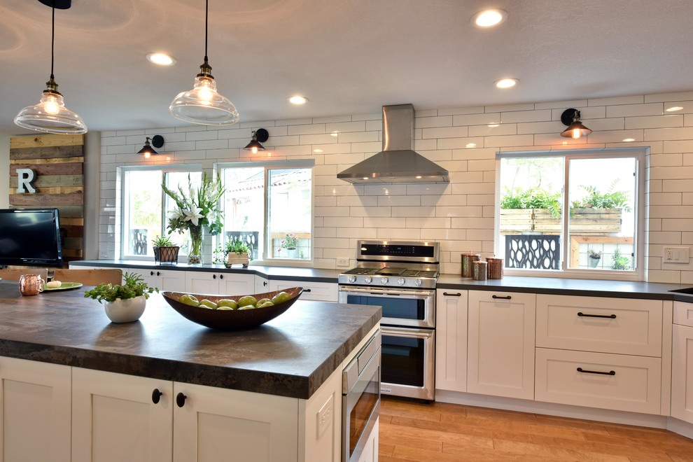 Large industrial u-shaped open plan kitchen in Tampa with a single-bowl sink, shaker cabinets, white cabinets, quartz benchtops, white splashback, subway tile splashback, stainless steel appliances, light hardwood floors, with island and brown floor.