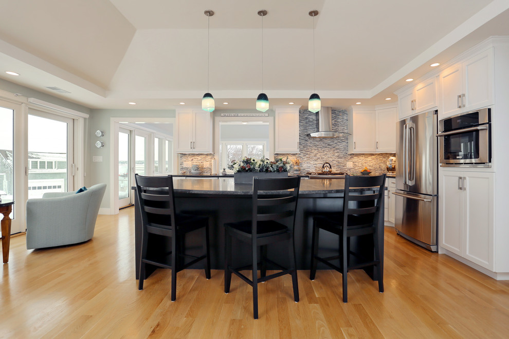 Inspiration for a mid-sized transitional l-shaped light wood floor open concept kitchen remodel in Boston with an undermount sink, shaker cabinets, white cabinets, granite countertops, gray backsplash, matchstick tile backsplash, stainless steel appliances and an island