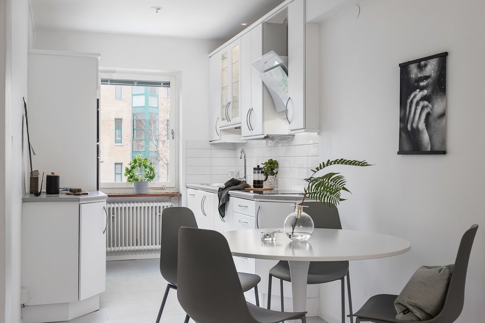 Inspiration for a scandinavian galley eat-in kitchen in Malmo with an undermount sink, flat-panel cabinets, white cabinets, white splashback, white appliances, bamboo floors, no island, white floor and grey benchtop.