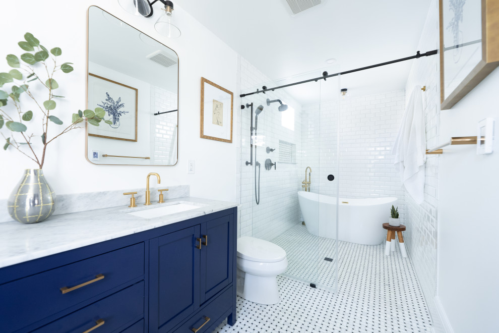 Inspiration for a mid-sized transitional master bathroom in Baltimore with shaker cabinets, blue cabinets, a freestanding tub, a curbless shower, a two-piece toilet, white tile, ceramic tile, white walls, marble floors, an undermount sink, marble benchtops, grey floor, a sliding shower screen, grey benchtops, a double vanity and a freestanding vanity.