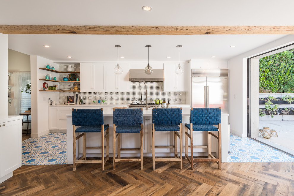This is an example of a beach style galley kitchen in Los Angeles with shaker cabinets, white cabinets, multi-coloured splashback, mirror splashback, stainless steel appliances, cement tiles, with island and multi-coloured floor.